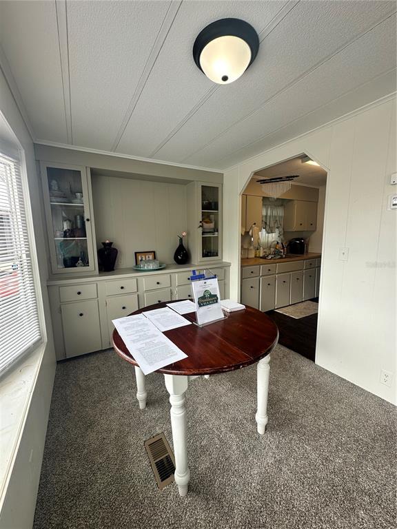 A dining area features a round wooden table, built-in cabinetry, and carpeted flooring — 6433 JACARANDA AVENUE NE, WINTER HAVEN, FL