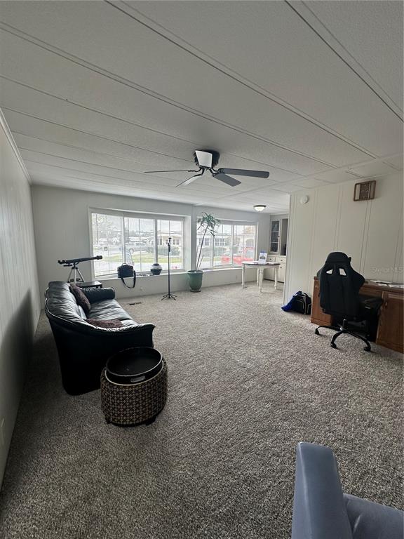 A living room with carpeted floors, a black sofa, a desk, and large windows — 6433 JACARANDA AVENUE NE, WINTER HAVEN, FL