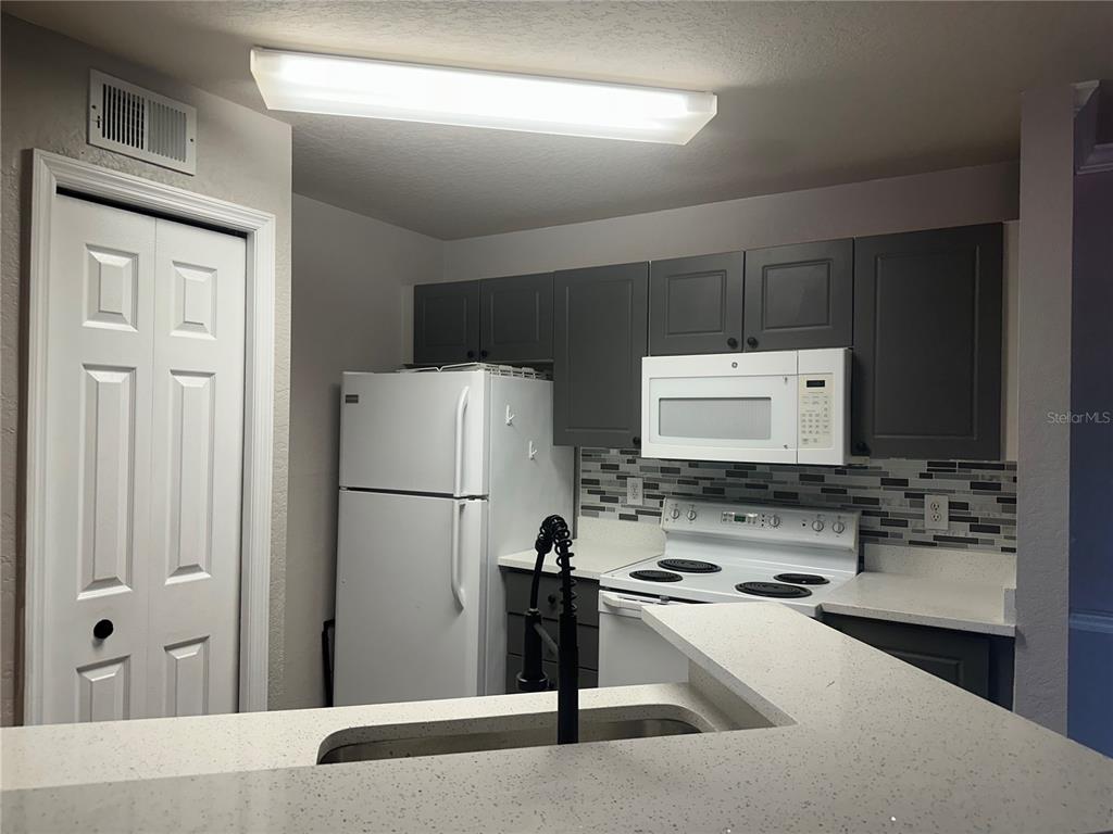 A kitchen features gray cabinets, white appliances, a tiled backsplash, and a white countertop — 4209 WOODSTORKS WALK WAY UNIT 1205, LUTZ, FL