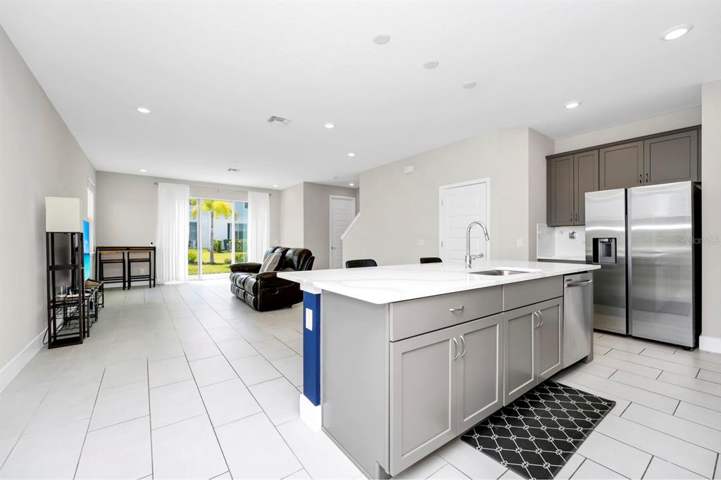 A modern kitchen with a gray island and stainless steel appliances overlooks a living area — 743 DRIVING RANGE COURT, REUNION, FL