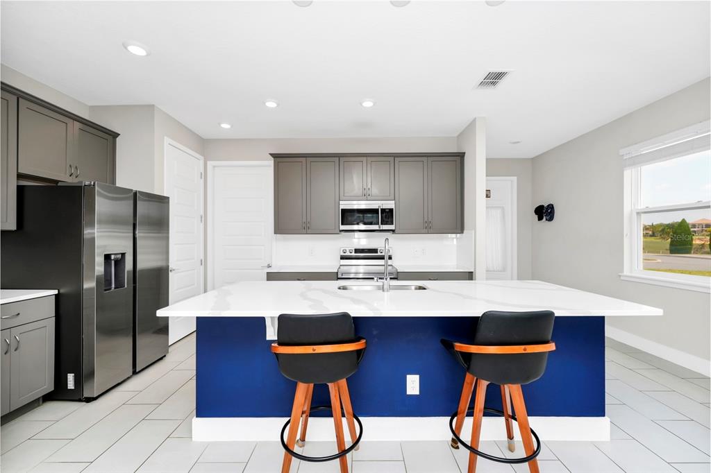 A modern kitchen features a blue island, white countertops, gray cabinets, and stainless steel appliances — 743 DRIVING RANGE COURT, REUNION, FL