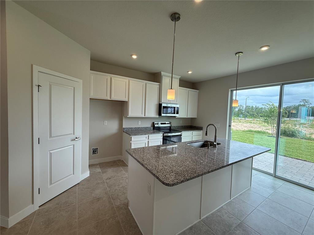 A kitchen featuring white cabinets, granite countertops, a center island, and a sliding glass door — 1235 PINEYWOOD FIELD DRIVE, DAVENPORT, FL