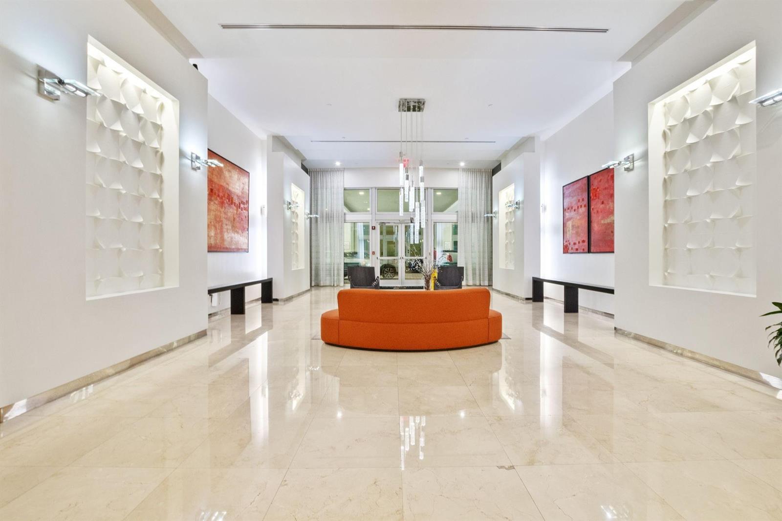 A bright, modern lobby features a curved orange sofa, marble floors, and textured wall art — 9066 SW 73rd Court # 701, Miami FL 33156, MIAMI, FL