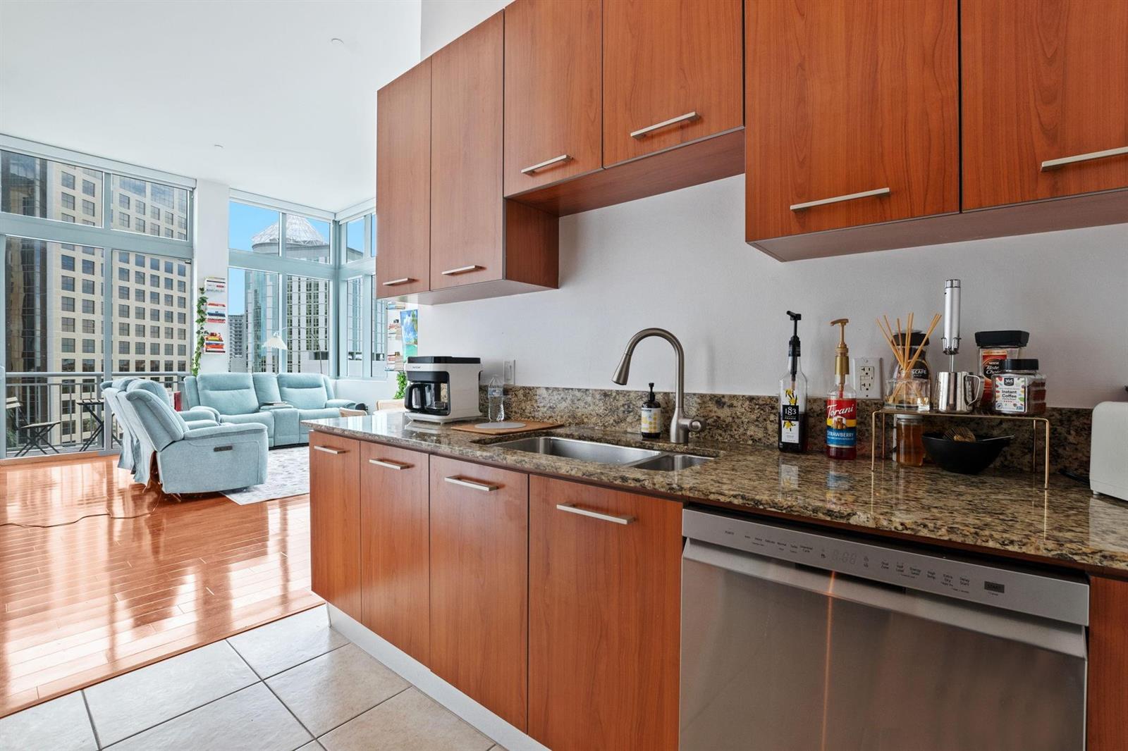 A kitchen with wood cabinets, granite countertops, and a stainless steel dishwasher overlooks a living area — 9066 SW 73rd Court # 701, Miami FL 33156, MIAMI, FL