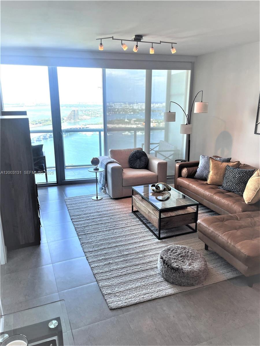 A living room features a leather sectional, glass coffee table, and floor-to-ceiling windows with water views — 888 Biscayne Blvd # 4310, Miami FL 33132, MIAMI, FL
