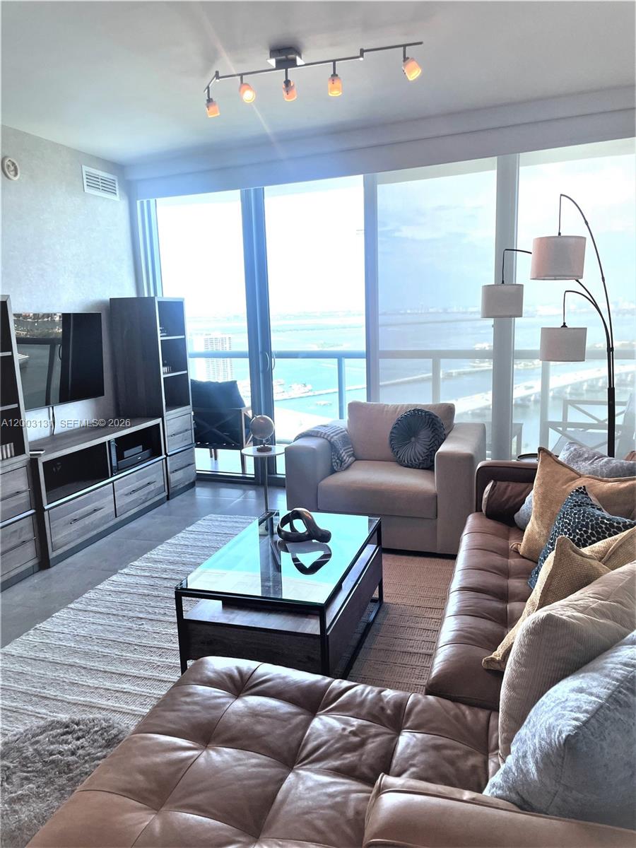A living room features a leather sofa, glass coffee table, and floor-to-ceiling windows overlooking water — 888 Biscayne Blvd # 4310, Miami FL 33132, MIAMI, FL