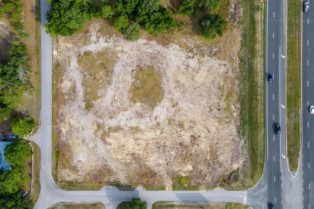 An aerial view shows a cleared, rectangular vacant lot bordered by roads and trees — US HWY 441/9520 SE 156TH PL, SUMMERFIELD, FL