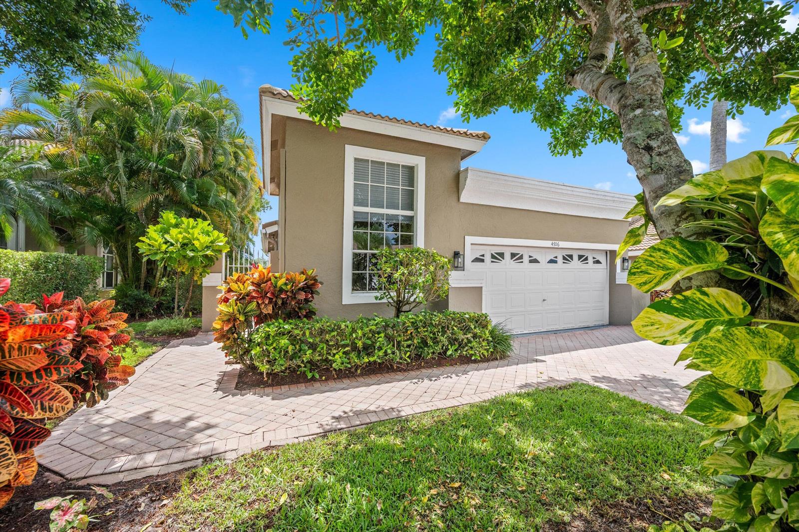 A tan house with a white garage door and a paved driveway surrounded by landscaping — 4706 Carlton Golf Drive, Lake Worth FL 33449, LAKE WORTH, FL