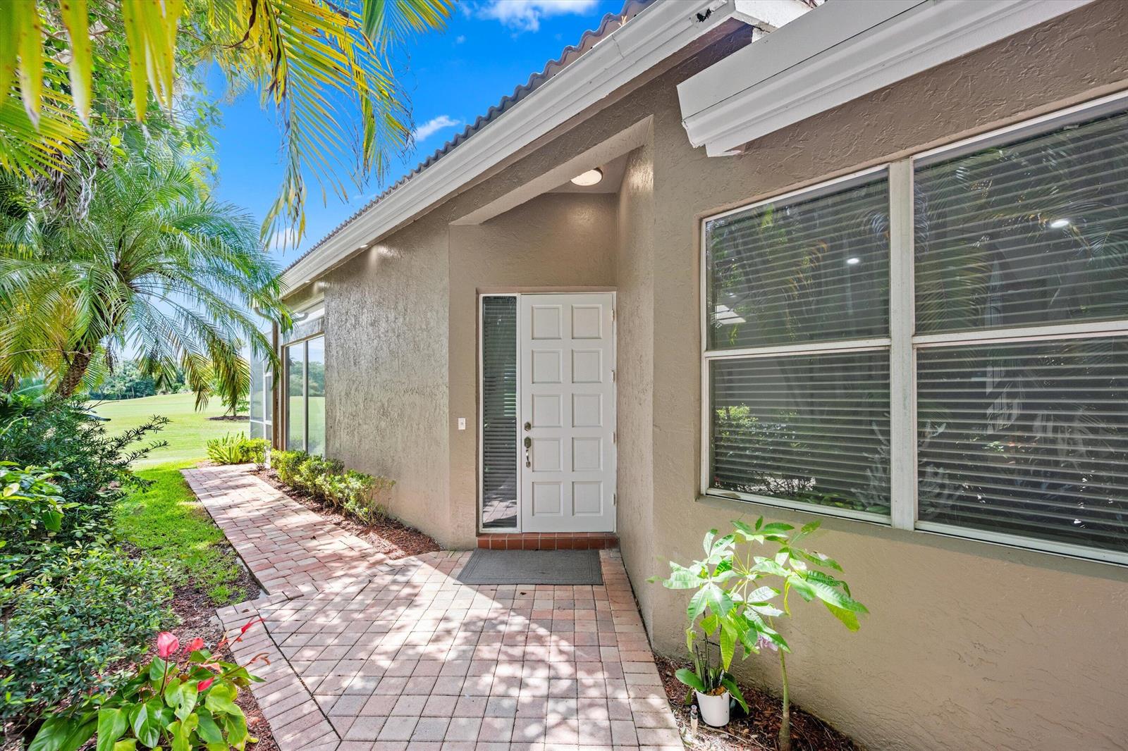 A white front door with a side window sits on a brick walkway beside a house — 4706 Carlton Golf Drive, Lake Worth FL 33449, LAKE WORTH, FL