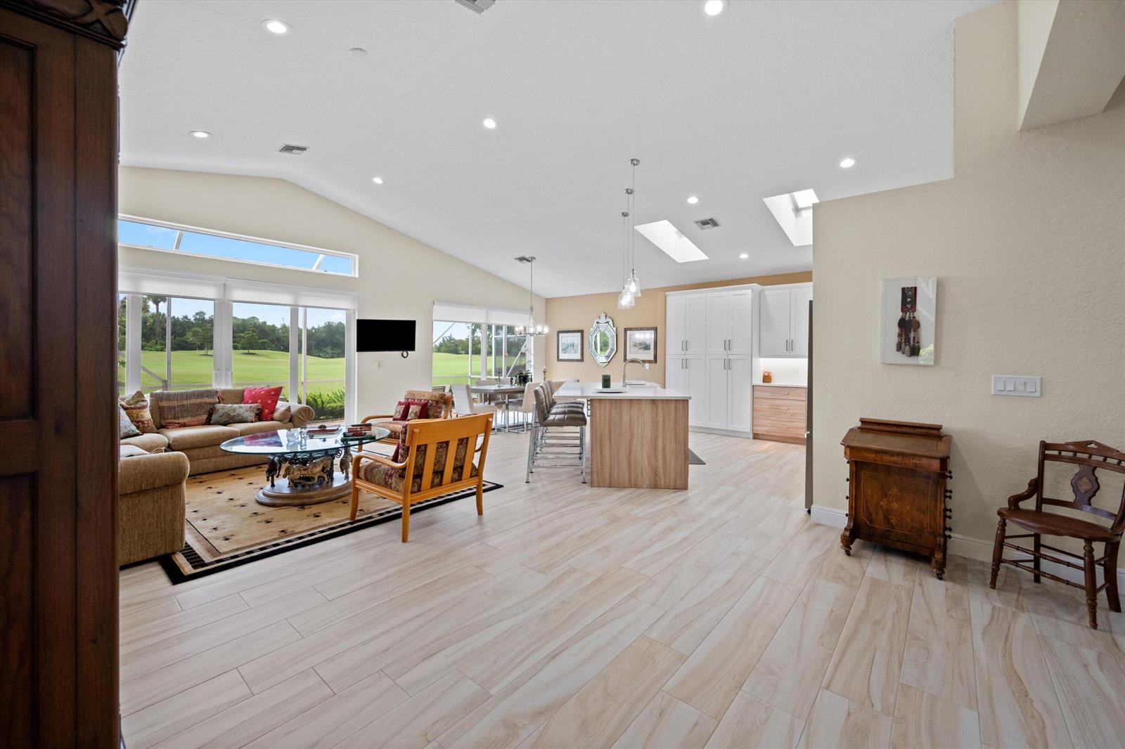 An open-concept living room and kitchen feature vaulted ceilings, light wood flooring, and large windows — 4706 Carlton Golf Drive, Lake Worth FL 33449, LAKE WORTH, FL