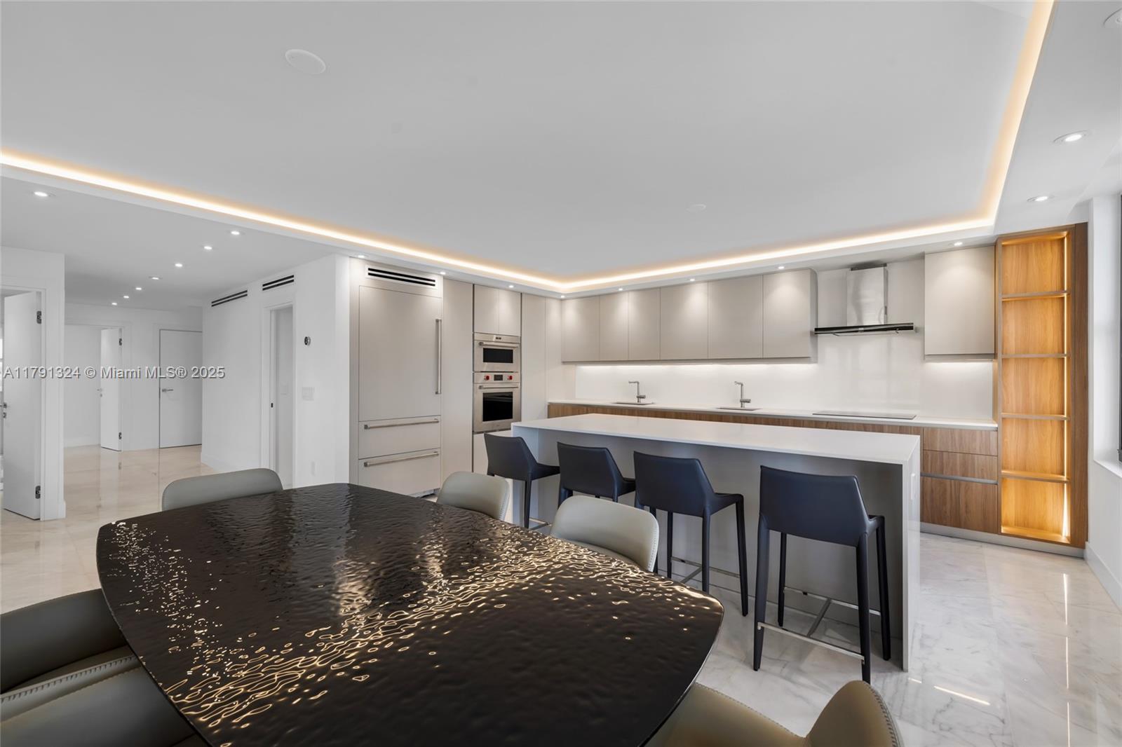 A modern kitchen features a large island, dark bar stools, and a textured dining table — 9801 Collins Ave # 17R, Bal Harbour FL 33154, BAL HARBOUR, FL