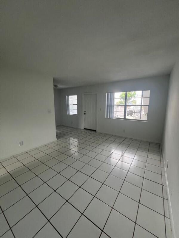 An empty room with white walls and white tiled flooring featuring dark grout lines — COCONUT CREEK, FL