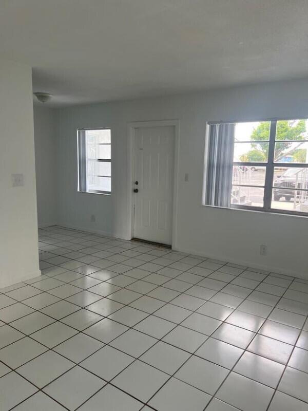 An empty room with white walls, white tile flooring, and a white entry door — COCONUT CREEK, FL