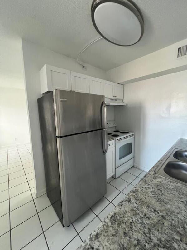 A kitchen features stainless steel appliances, white cabinets, granite countertops, and white tiled flooring — COCONUT CREEK, FL