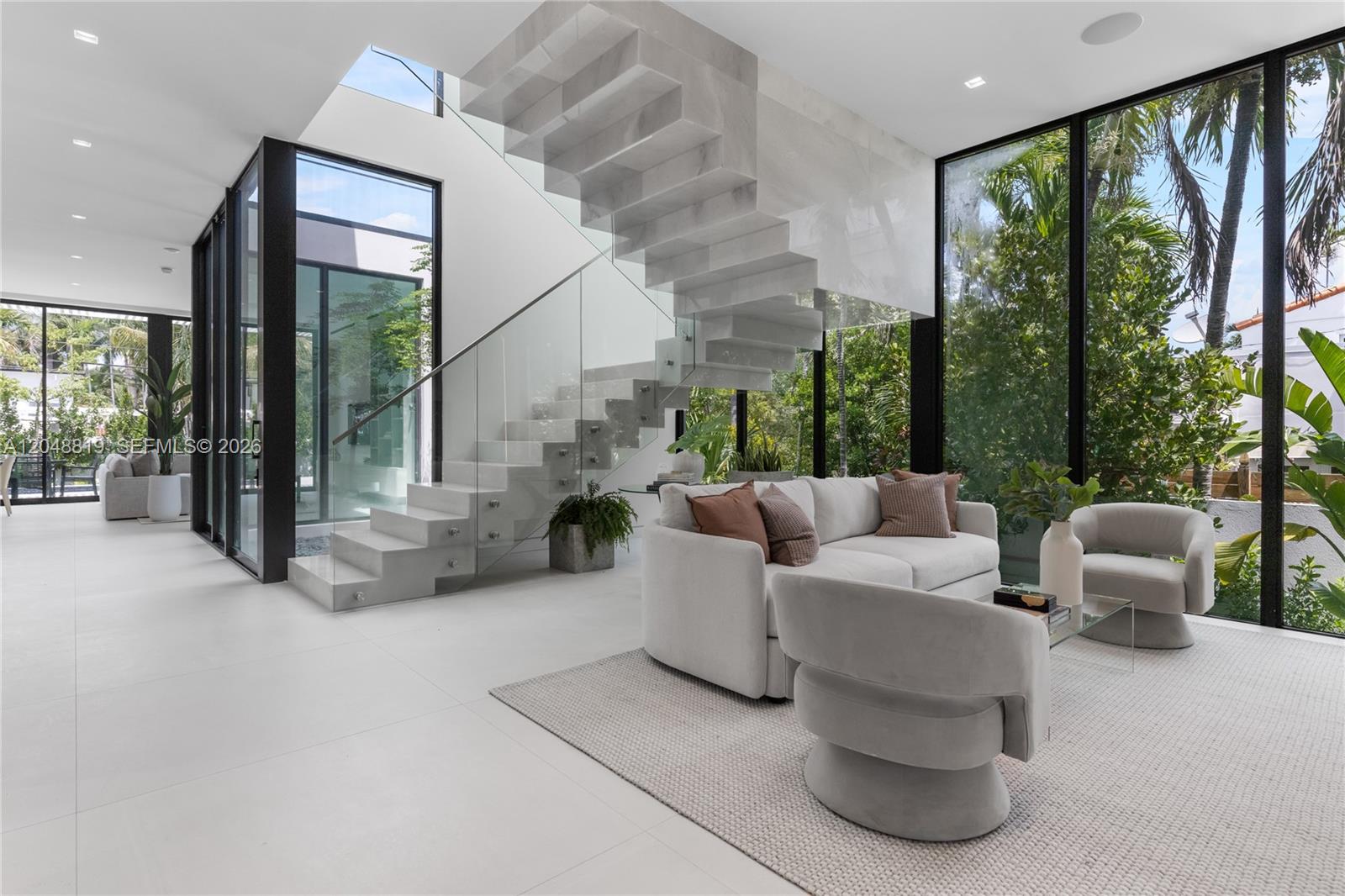 A modern living room features a floating stone staircase, floor-to-ceiling windows, and white tile flooring — 4504 Sheridan Ave, Miami Beach FL 33140, MIAMI BEACH, FL