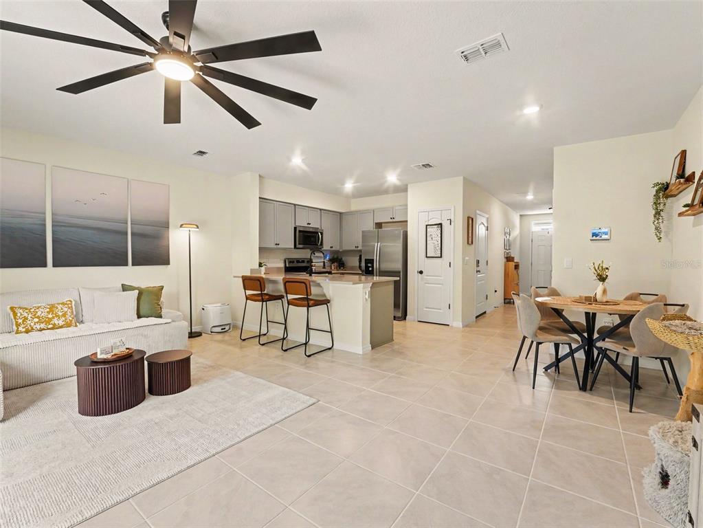 An open-concept living room and kitchen feature light tile flooring and a ceiling fan — 2356 PENGUIN BOULEVARD, DAVENPORT, FL