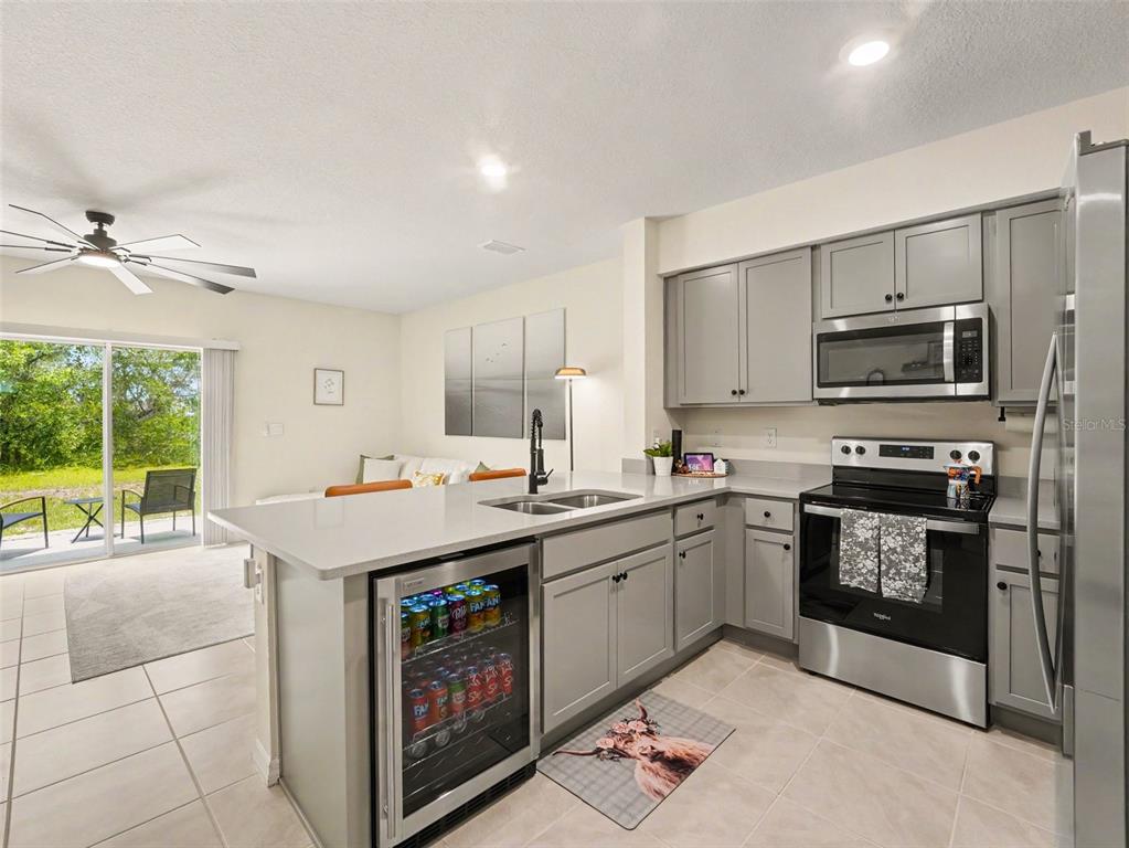 A kitchen with gray cabinets, stainless steel appliances, a beverage fridge, and an adjacent patio — 2356 PENGUIN BOULEVARD, DAVENPORT, FL