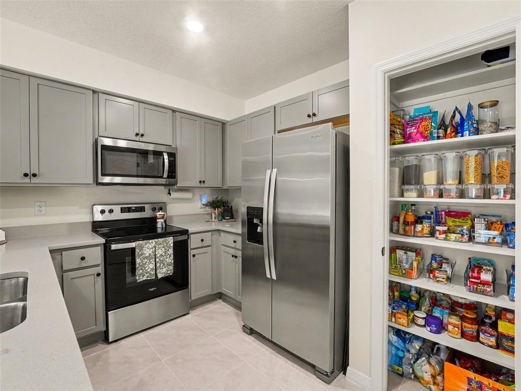 A kitchen features grey cabinets, stainless steel appliances, quartz countertops, and an open pantry — 2356 PENGUIN BOULEVARD, DAVENPORT, FL