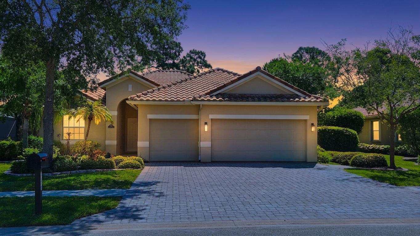 A single-story house with a tiled roof, two-car garage, and a paved driveway at dusk — 7677 Fieldstone Ranch Square, Vero Beach FL 32967, VERO BEACH, FL