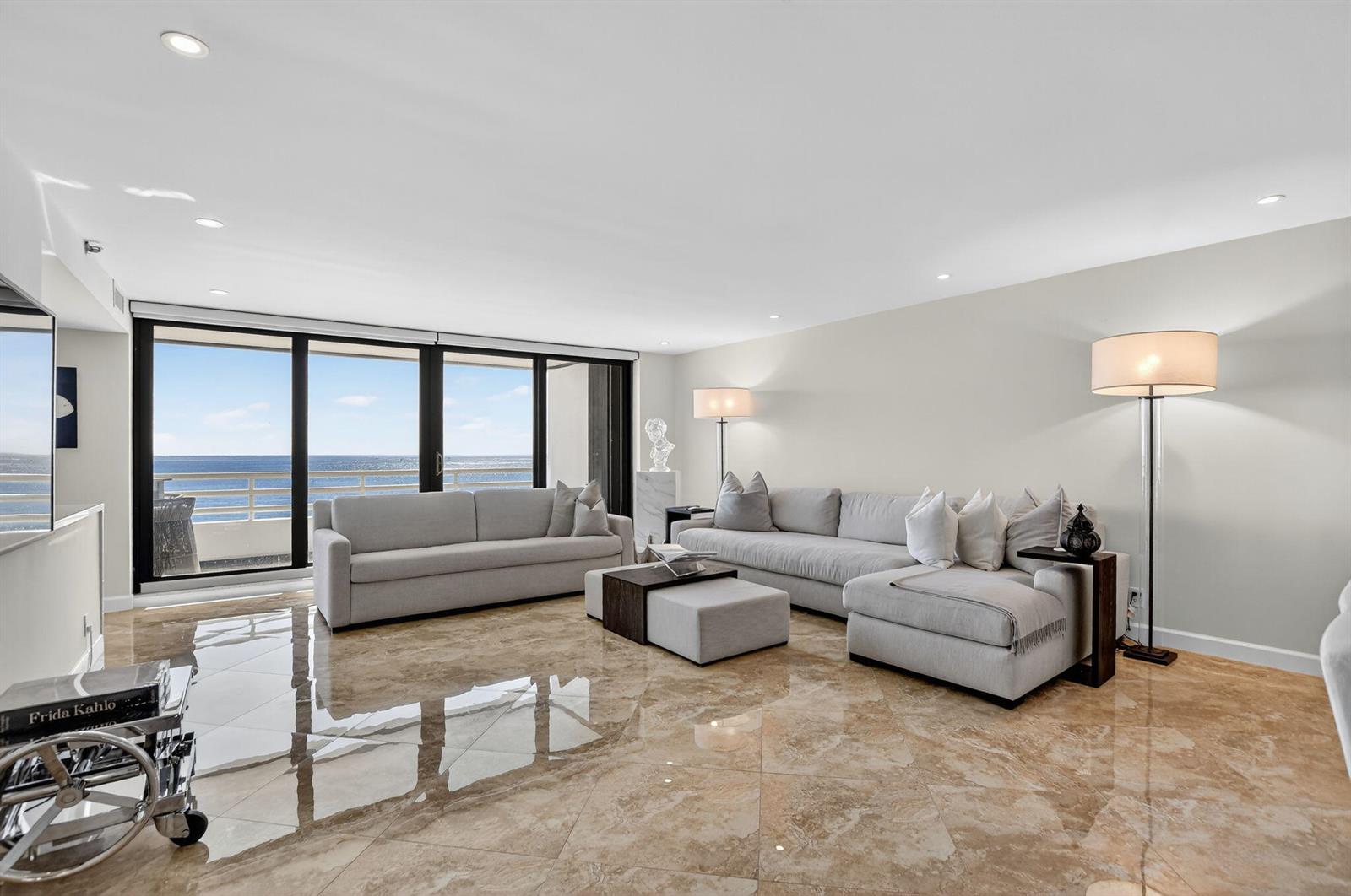 A living room features light gray sofas, marble tile flooring, and floor-to-ceiling windows overlooking water — 1500 S Ocean Boulevard # 704, Boca Raton FL 33432, BOCA RATON, FL