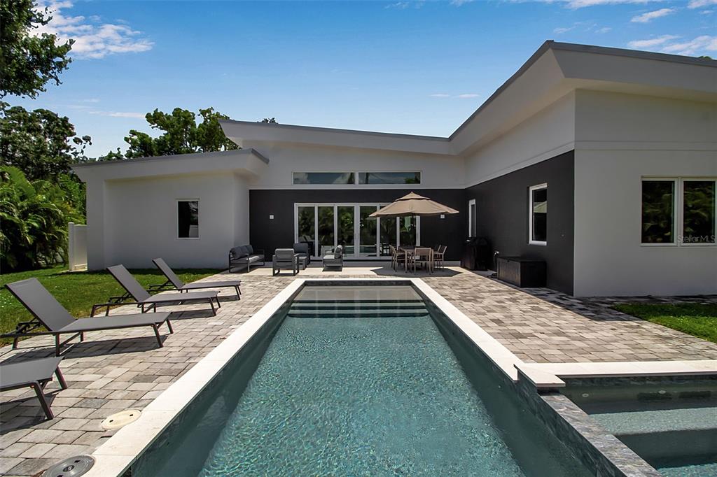 A modern house exterior features a rectangular swimming pool, stone patio, and outdoor dining area — 2231 WOOD STREET, SARASOTA, FL