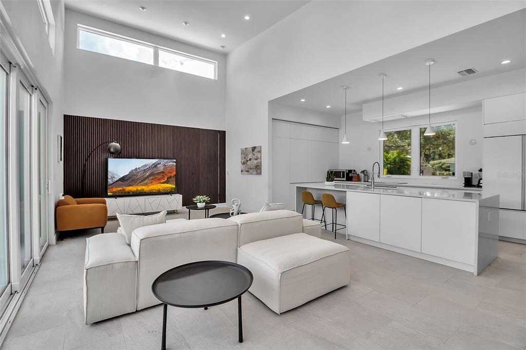 A modern open-concept living room and kitchen featuring white cabinetry, a sectional sofa, and wood-slatted wall — 2231 WOOD STREET, SARASOTA, FL