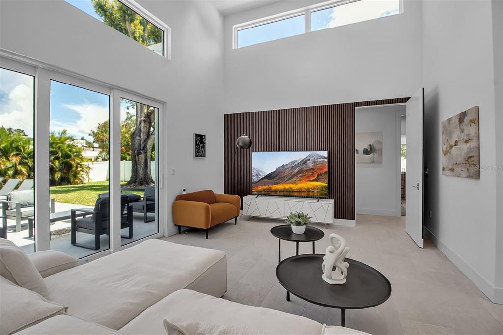 A modern living room features high ceilings, a slatted wood accent wall, and sliding glass doors — 2231 WOOD STREET, SARASOTA, FL