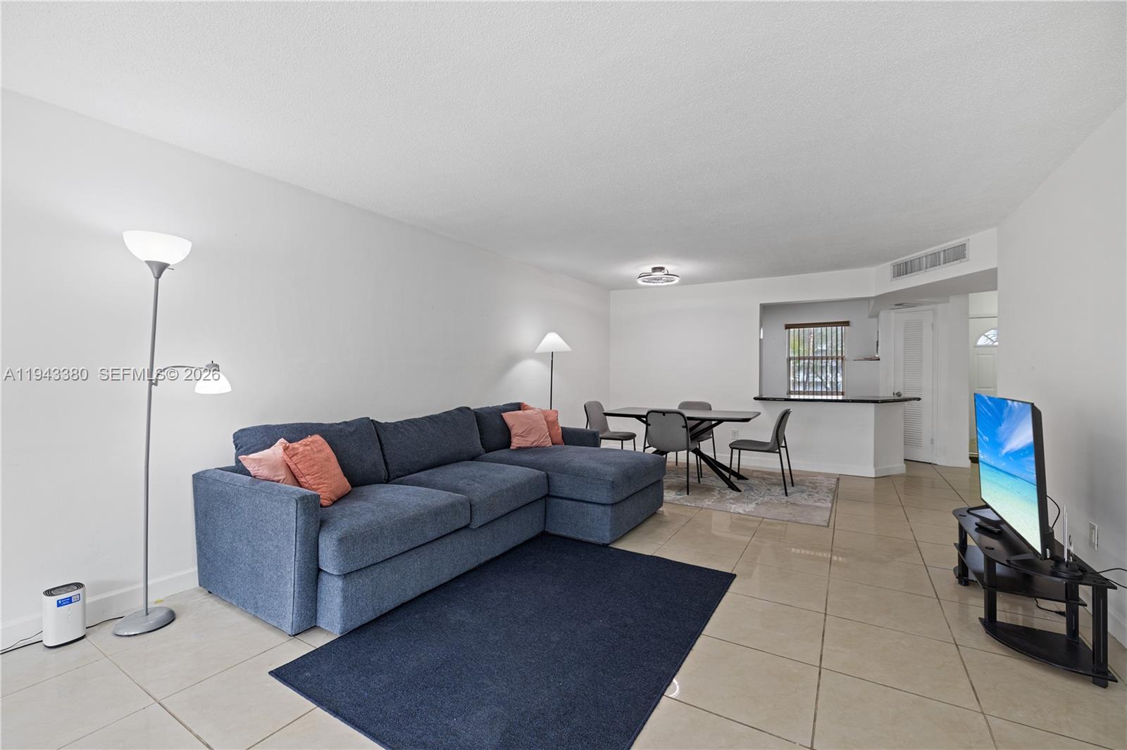 A living room with a blue sectional sofa, dining area, and tile flooring — 1501 NE 191st St # C216, Miami FL 33179, MIAMI, FL
