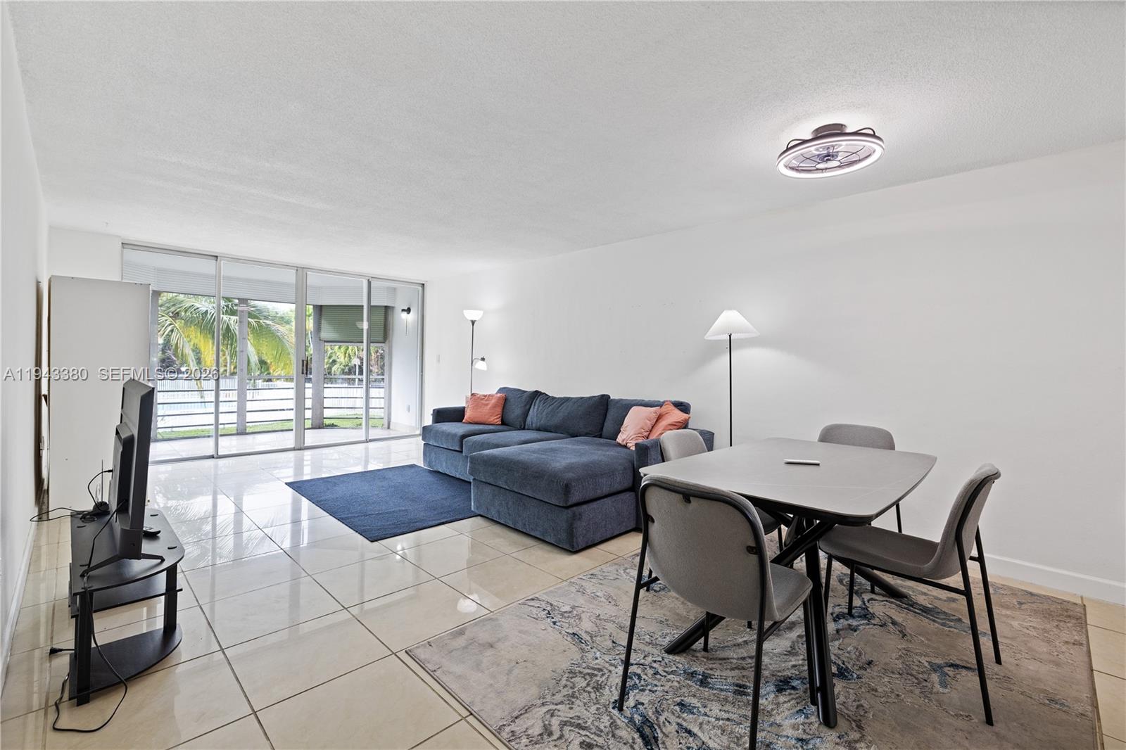 A living and dining area features tile floors, a blue sectional, and a glass balcony door — 1501 NE 191st St # C216, Miami FL 33179, MIAMI, FL