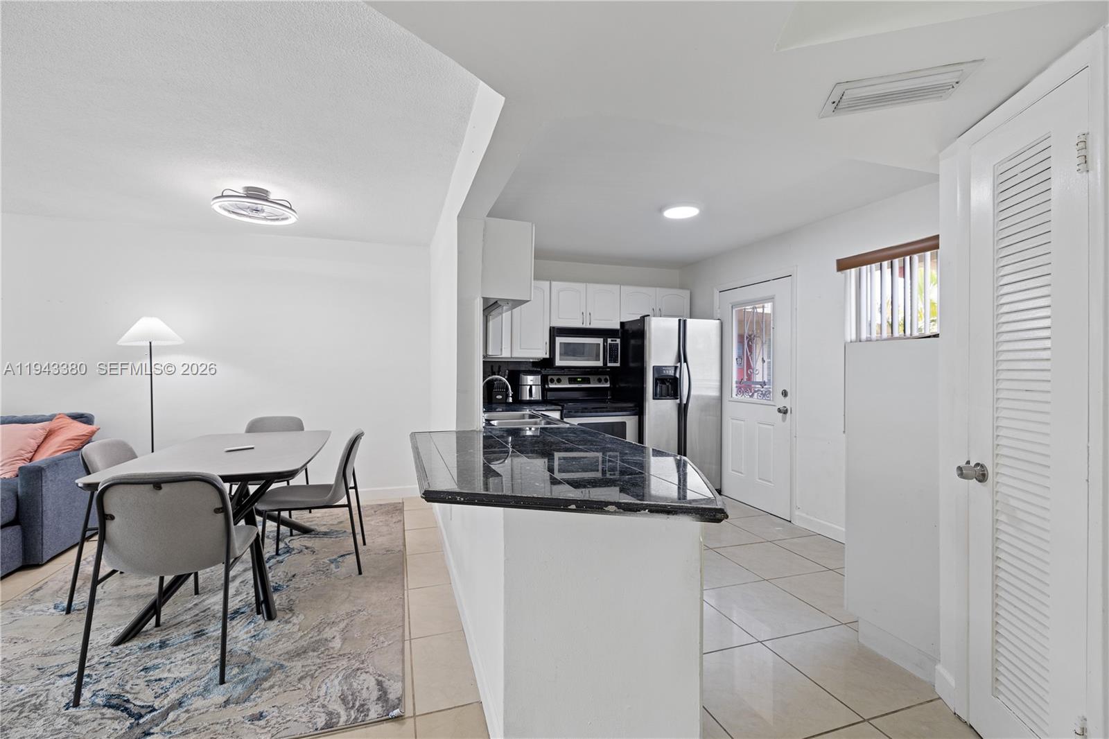 A kitchen with dark granite countertops and white cabinets opens to a dining area — 1501 NE 191st St # C216, Miami FL 33179, MIAMI, FL