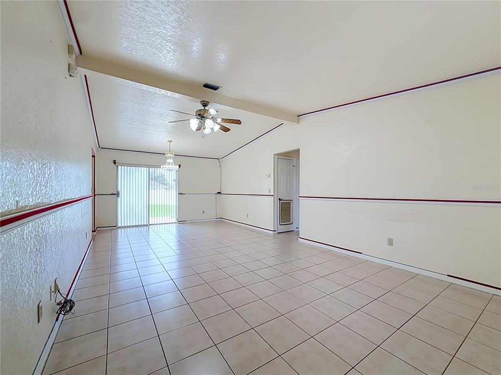 An empty living room features light-colored floor tiles, a vaulted ceiling, and red wall trim — 2939 SW 144TH PLACE ROAD, OCALA, FL