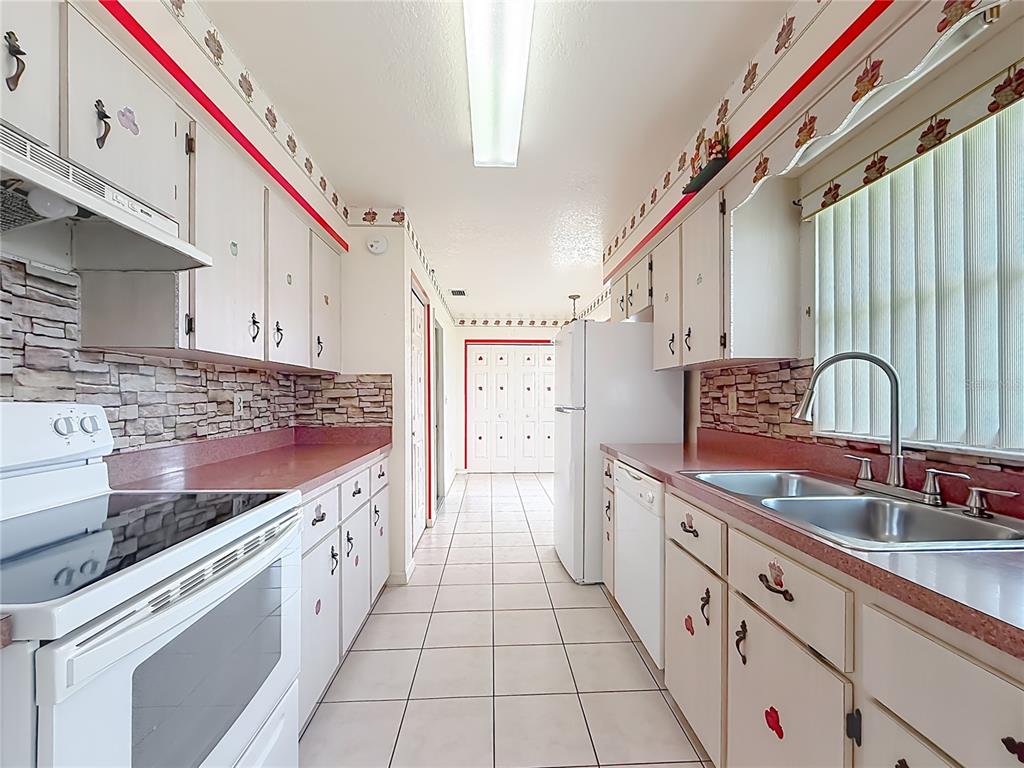 A galley kitchen features white cabinets, red countertops, stone-look backsplashes, and white tile flooring — 2939 SW 144TH PLACE ROAD, OCALA, FL