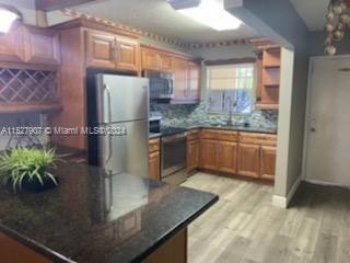 A kitchen features wood cabinets, stainless steel appliances, a dark countertop, and light wood flooring — 5500 SW 77th Ct # 201, Miami FL 33155, MIAMI, FL