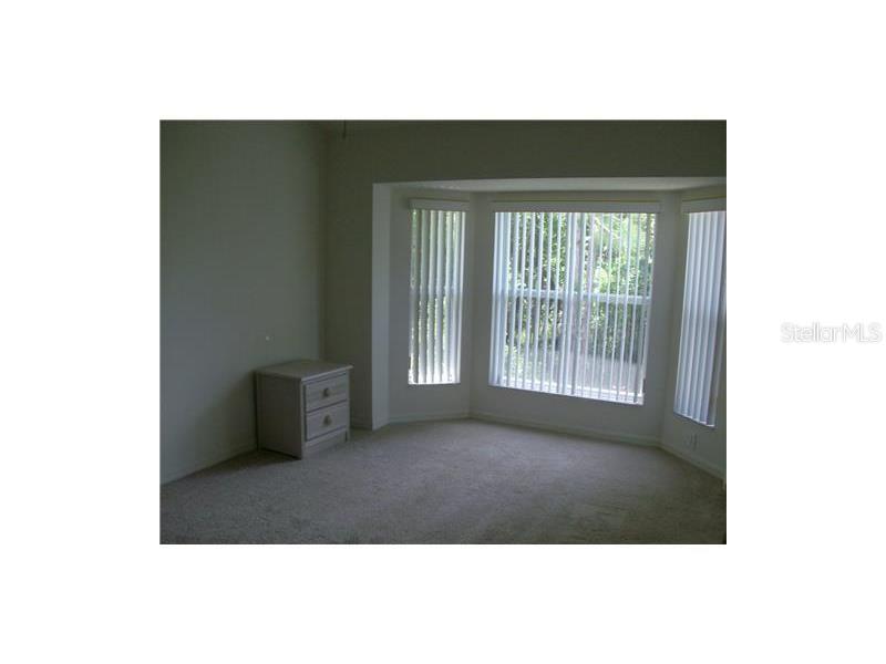 A bedroom with beige carpet, light-colored walls, and a bay window with vertical blinds — 4645 TOWER HILL LANE UNIT 2521, SARASOTA, FL