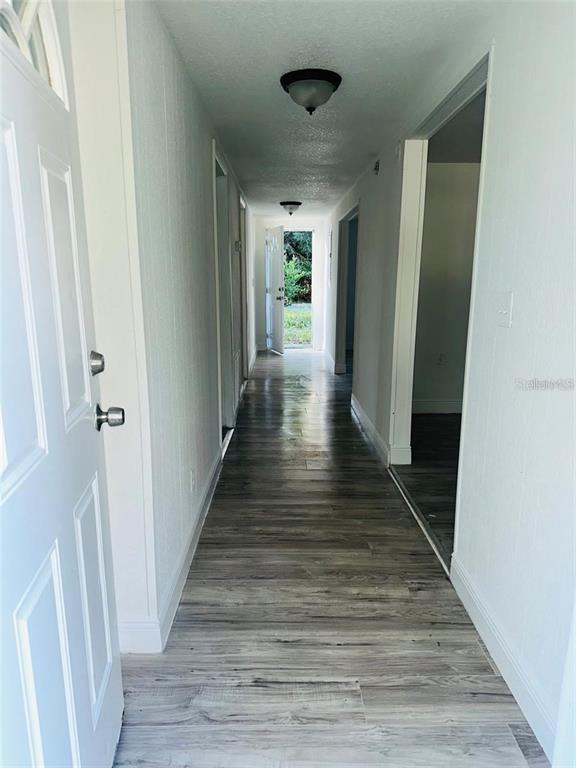 A hallway with light wood-look flooring leads to an open exterior door — 10221 BEAM STREET, JACKSONVILLE, FL