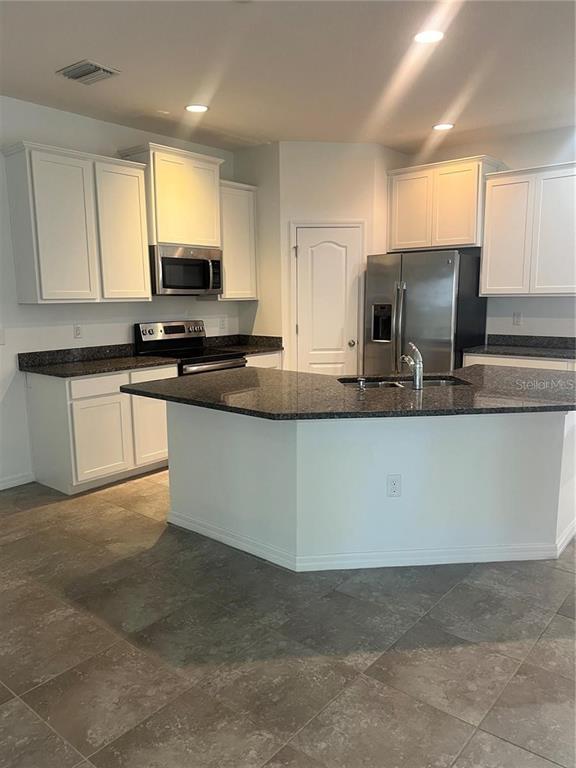 A kitchen features white cabinets, dark granite countertops, stainless steel appliances, and tile flooring — 32995 WINDELSTRAW DRIVE, WESLEY CHAPEL, FL