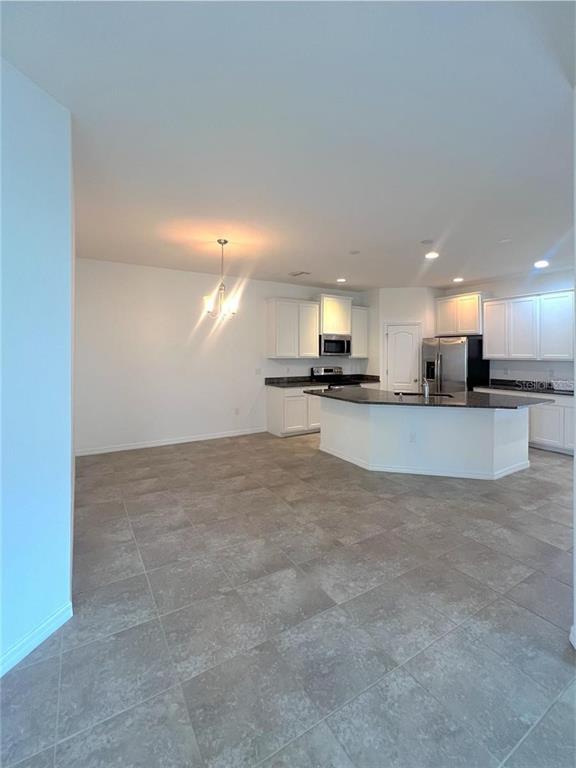 A kitchen with white cabinets, a dark island, and tile flooring opens to a dining area — 32995 WINDELSTRAW DRIVE, WESLEY CHAPEL, FL