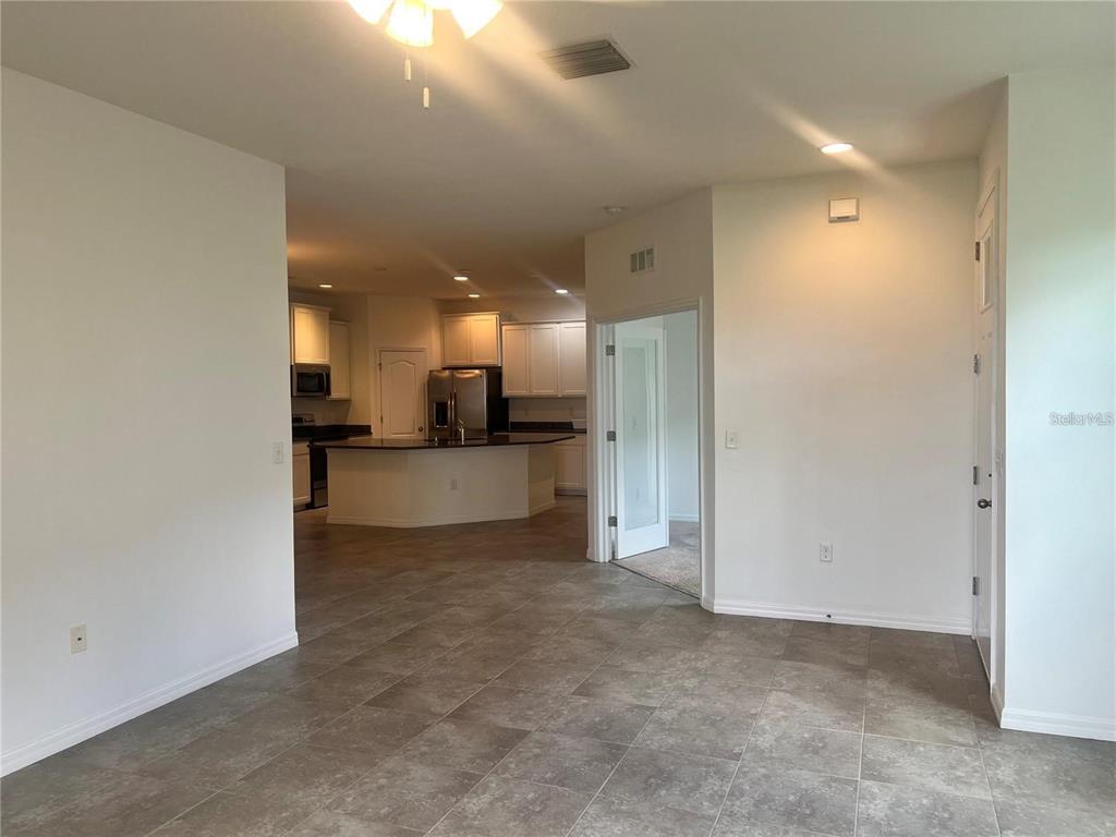 An open-concept room with gray tile flooring leads to a kitchen with white cabinets — 32995 WINDELSTRAW DRIVE, WESLEY CHAPEL, FL