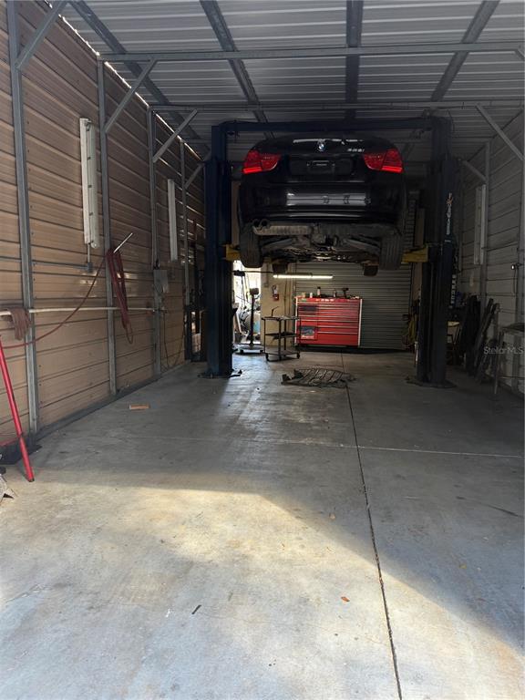A car is elevated on a lift inside a metal-walled garage with a concrete floor — 906 SHADICK DRIVE, ORANGE CITY, FL