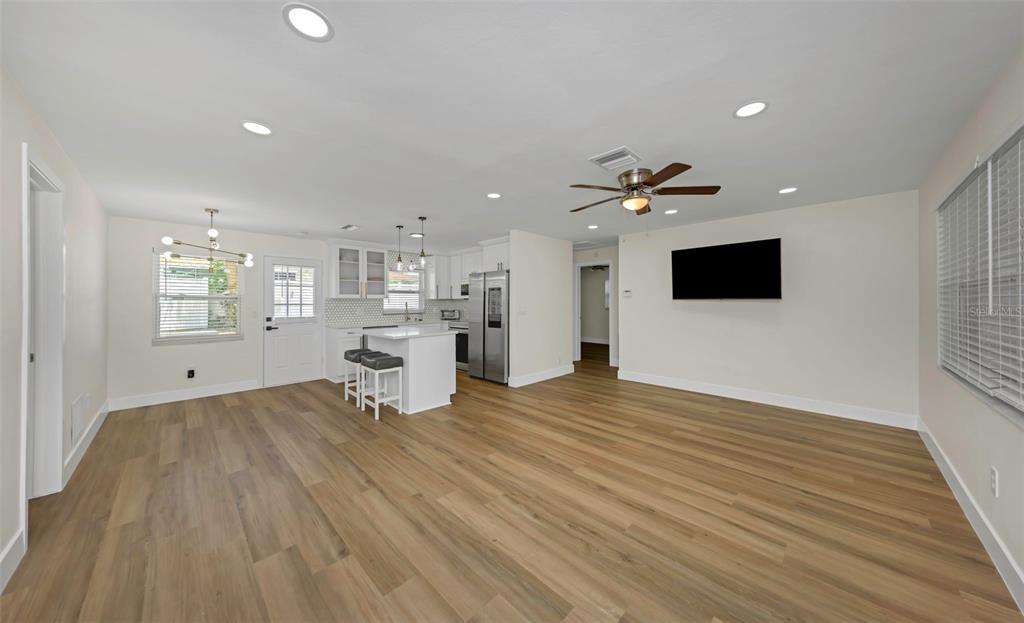 An open-concept living room and kitchen featuring light wood-look flooring and white cabinetry — 1806 VANCOUVER DRIVE, CLEARWATER, FL