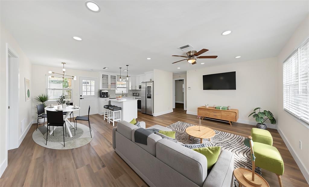 An open-concept living and dining area features light wood floors, white cabinetry, and modern furniture — 1806 VANCOUVER DRIVE, CLEARWATER, FL