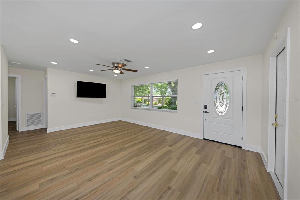 A living room with light-colored walls, wood-look flooring, a ceiling fan, and a front door — 1806 VANCOUVER DRIVE, CLEARWATER, FL