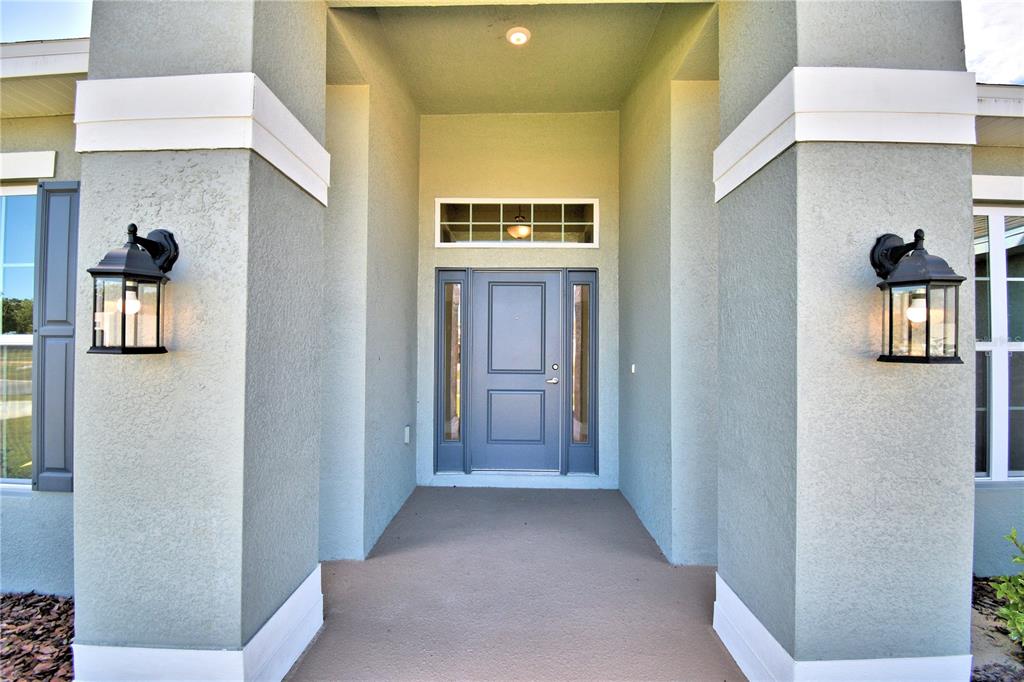 A covered entryway features a gray front door with sidelights and two black wall lanterns — 4425 JUNEBERRY DRIVE, AUBURNDALE, FL