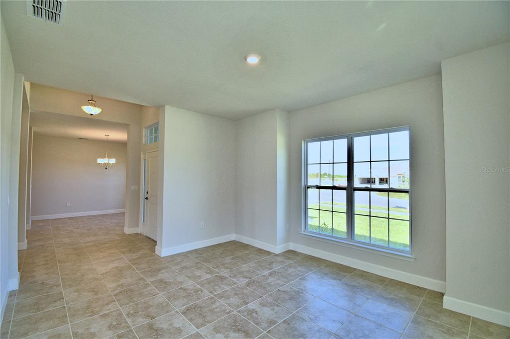 An empty room with tiled floors, a large window, and a view into an entryway — 4425 JUNEBERRY DRIVE, AUBURNDALE, FL
