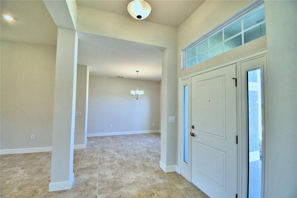 A bright entryway with tile flooring leads to a dining area with a chandelier — 4425 JUNEBERRY DRIVE, AUBURNDALE, FL