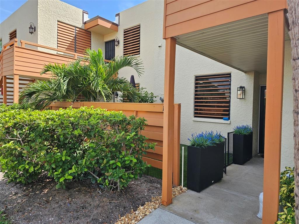 An exterior view of a multi-story building with a wooden fence, palm tree, and walkway — 153 WILD PALM DRIVE UNIT 1610, BRADENTON, FL