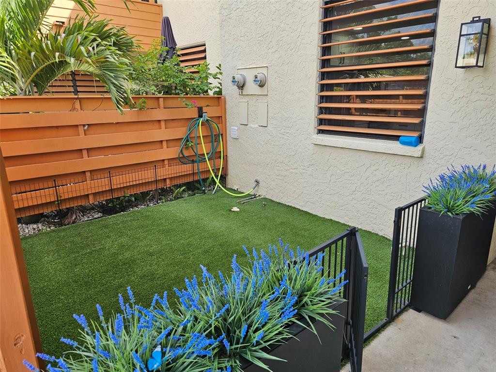 A small fenced patio features artificial turf, a wooden privacy screen, and potted blue flowers — 153 WILD PALM DRIVE UNIT 1610, BRADENTON, FL
