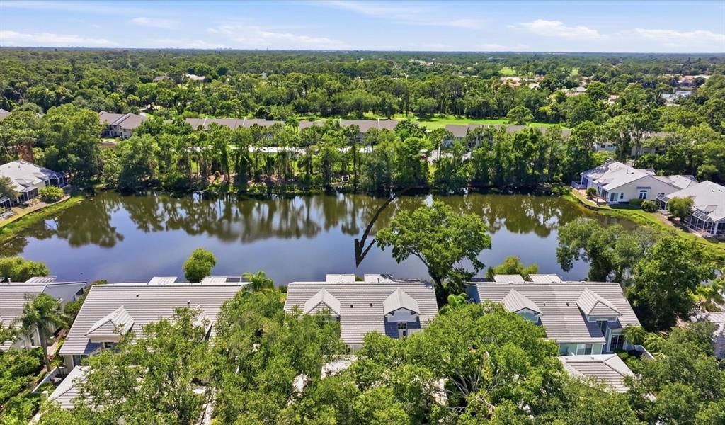 An aerial view shows townhomes situated along a lake with surrounding trees and landscaping — 7706 WHITEBRIDGE GLEN, UNIVERSITY PARK, FL
