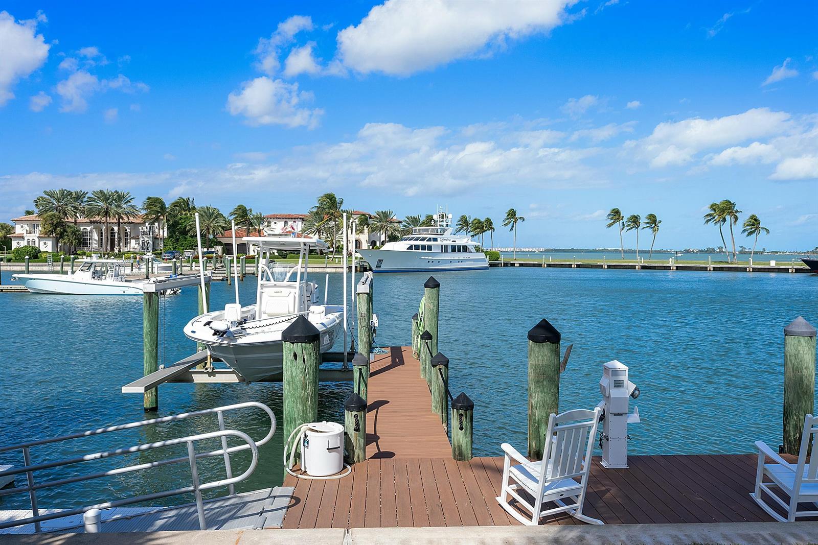 A wooden dock with rocking chairs extends into a canal featuring boats and palm trees — 6879 SE South Marina Way, Stuart FL 34996, STUART, FL