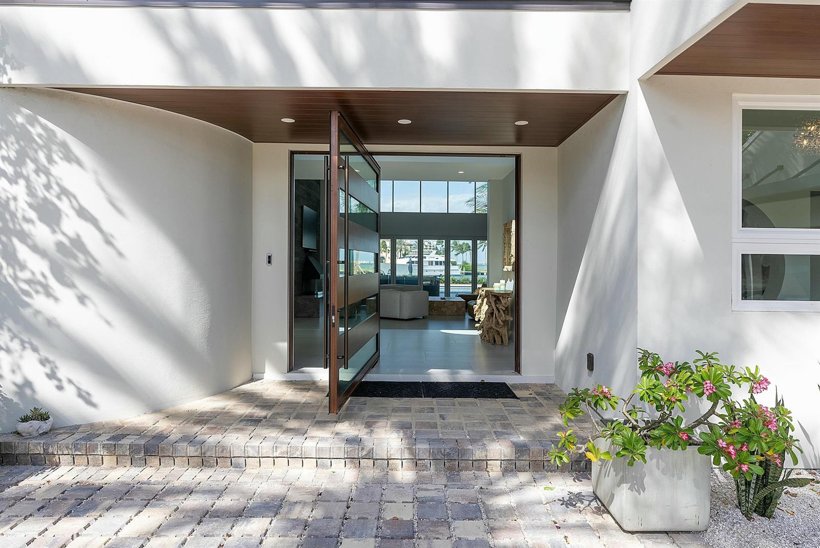 A modern home entrance features a large pivoting glass door and stone paver steps — 6879 SE South Marina Way, Stuart FL 34996, STUART, FL